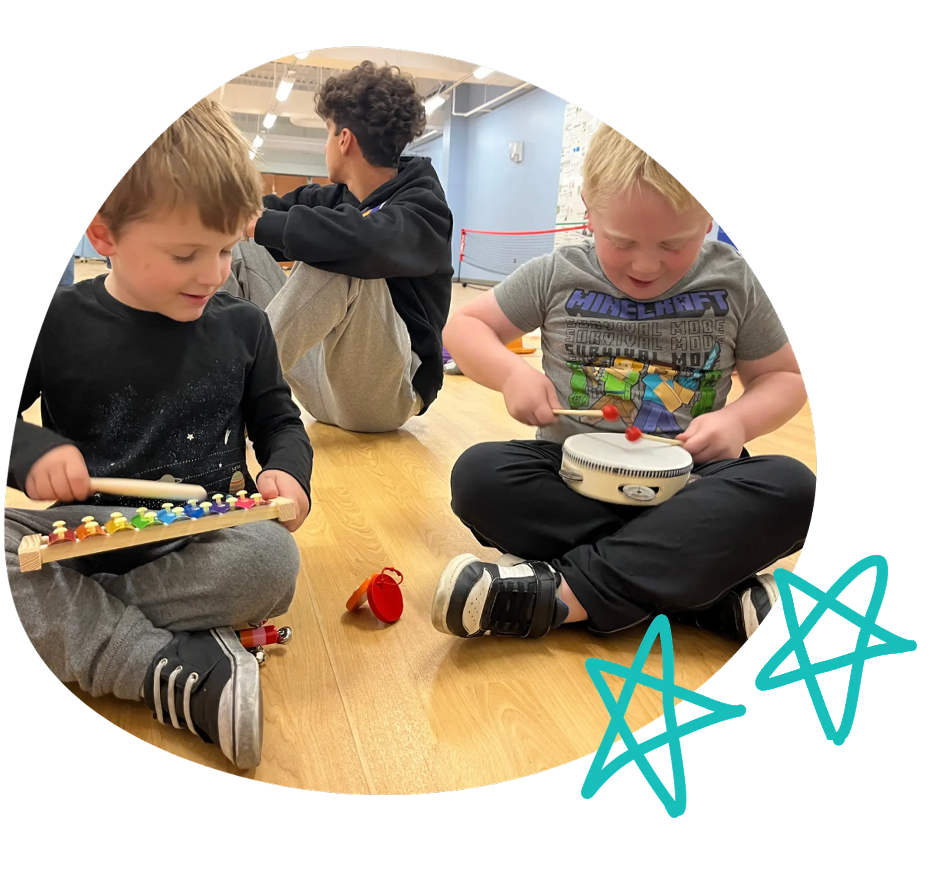 Two young children playing musical instruments together on a wooden floor during a music activity, smiling and focused.